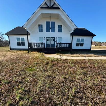 Modern two-story farmhouse with a white exterior and large front porch in a grassy landscape.