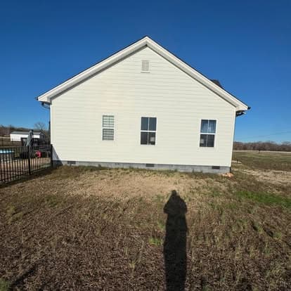 White house exterior with a fenced yard and clear blue sky, shadow visible on the ground.