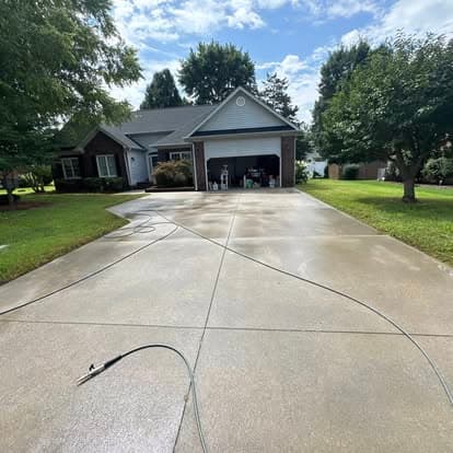 Clean, freshly washed concrete driveway leading to a house with a welcoming front yard.
