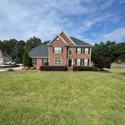 Brick two-story house with a manicured lawn and blue sky background.