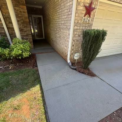 Concrete pathway leading to a home entrance with brick walls and greenery. House number 826.