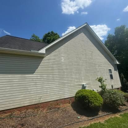 Side view of a single-story house with a clear blue sky and green landscaping.