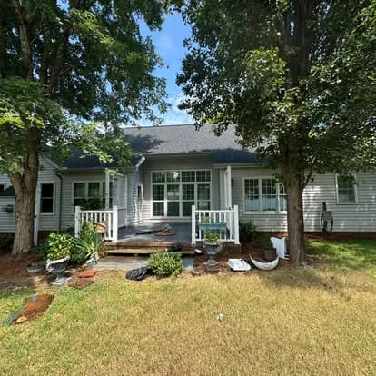 Cozy home exterior with porch, surrounded by trees and landscaped yard under blue sky.