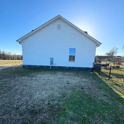 White residential house exterior with a window and fenced yard under a clear blue sky.
