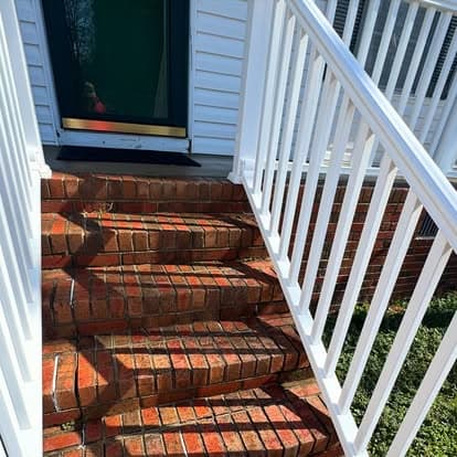 Brick stairs leading to a green door with white railings and shadow patterns.