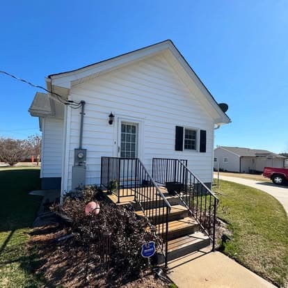 Charming white house with stairs, green lawn, and clear blue sky. Ideal for home buyers.