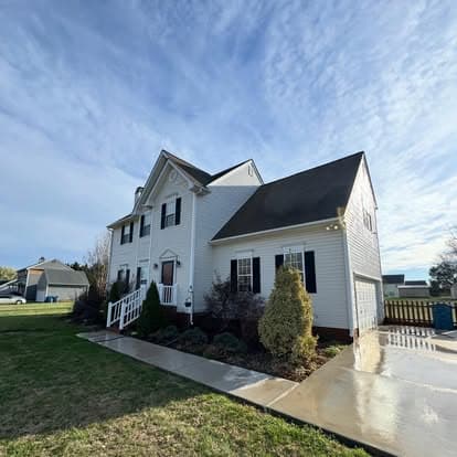 Two-story white house with a black roof, front lawn, and clear blue sky.