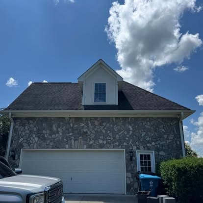 Stone house with a gable roof under a blue sky and fluffy clouds, parked vehicle in front.