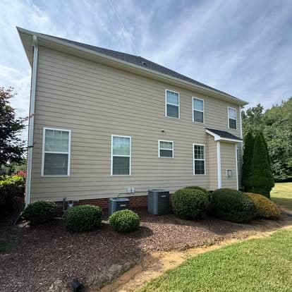 Side view of a modern two-story house with landscaped yard and HVAC units.
