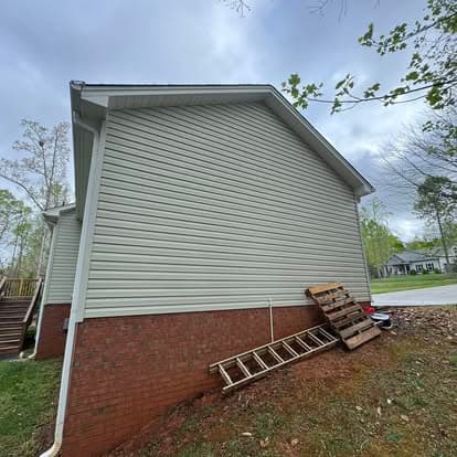 Side view of a home with vinyl siding, brick foundation, ladder, and driveway in the background.