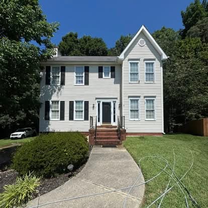 Two-story white house with black shutters and a landscaped front yard on a sunny day.